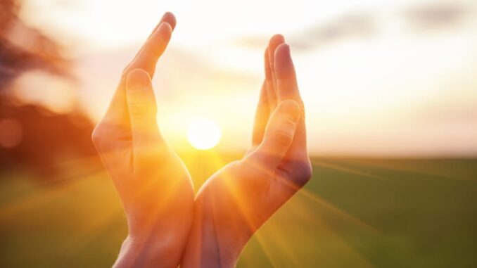 young woman raising hands praying at sunset or sunrise light